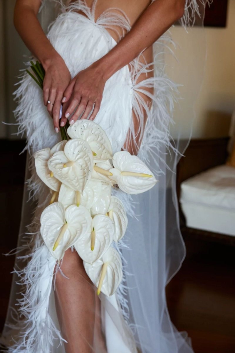 White anthurium wedding bouquet with feather-trimmed bridal gown and engagement ring detail