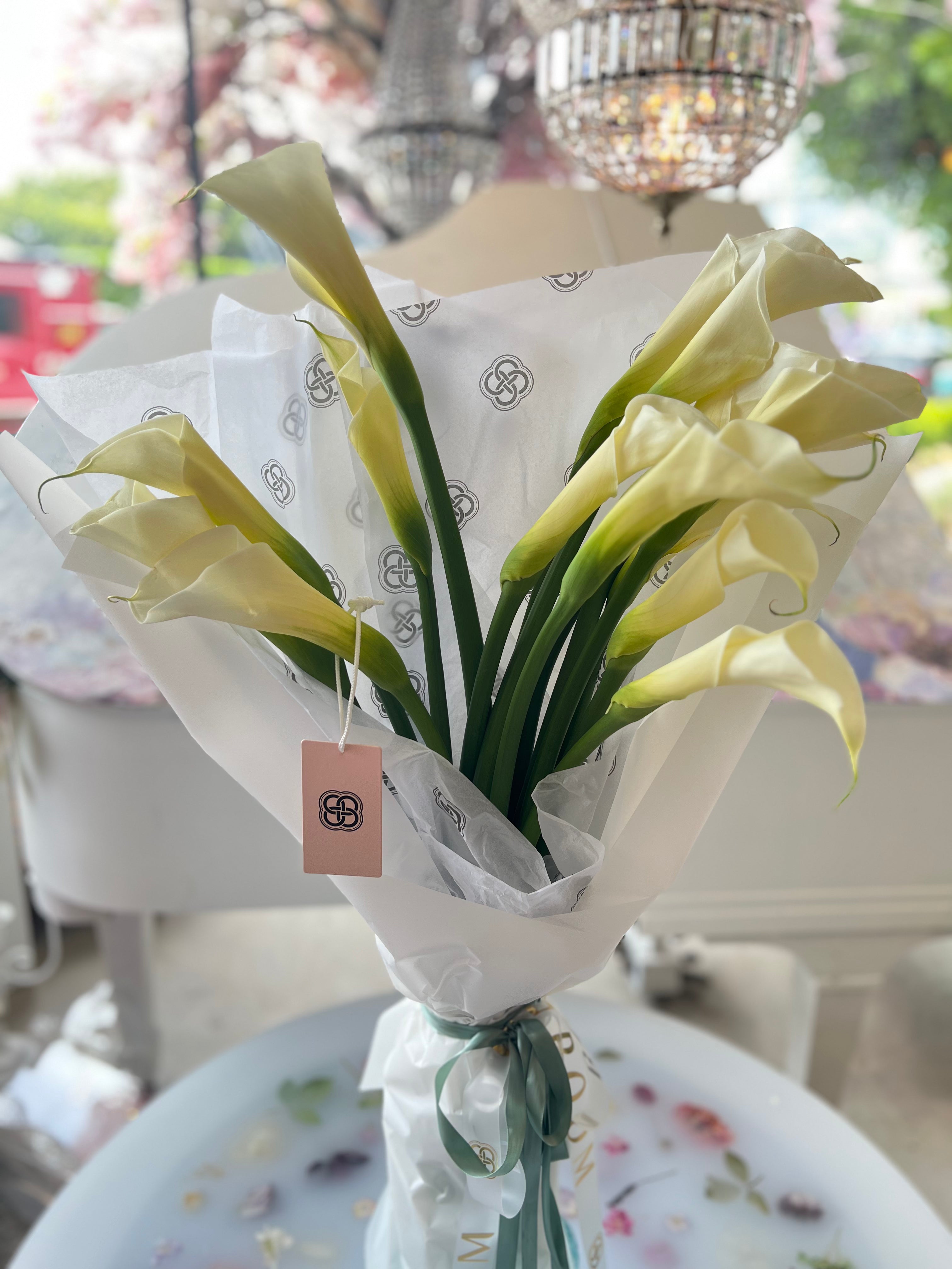 White calla lily bouquet wrapped in tissue paper with green ribbon from Los Angeles florist Bloom Boom Flowers