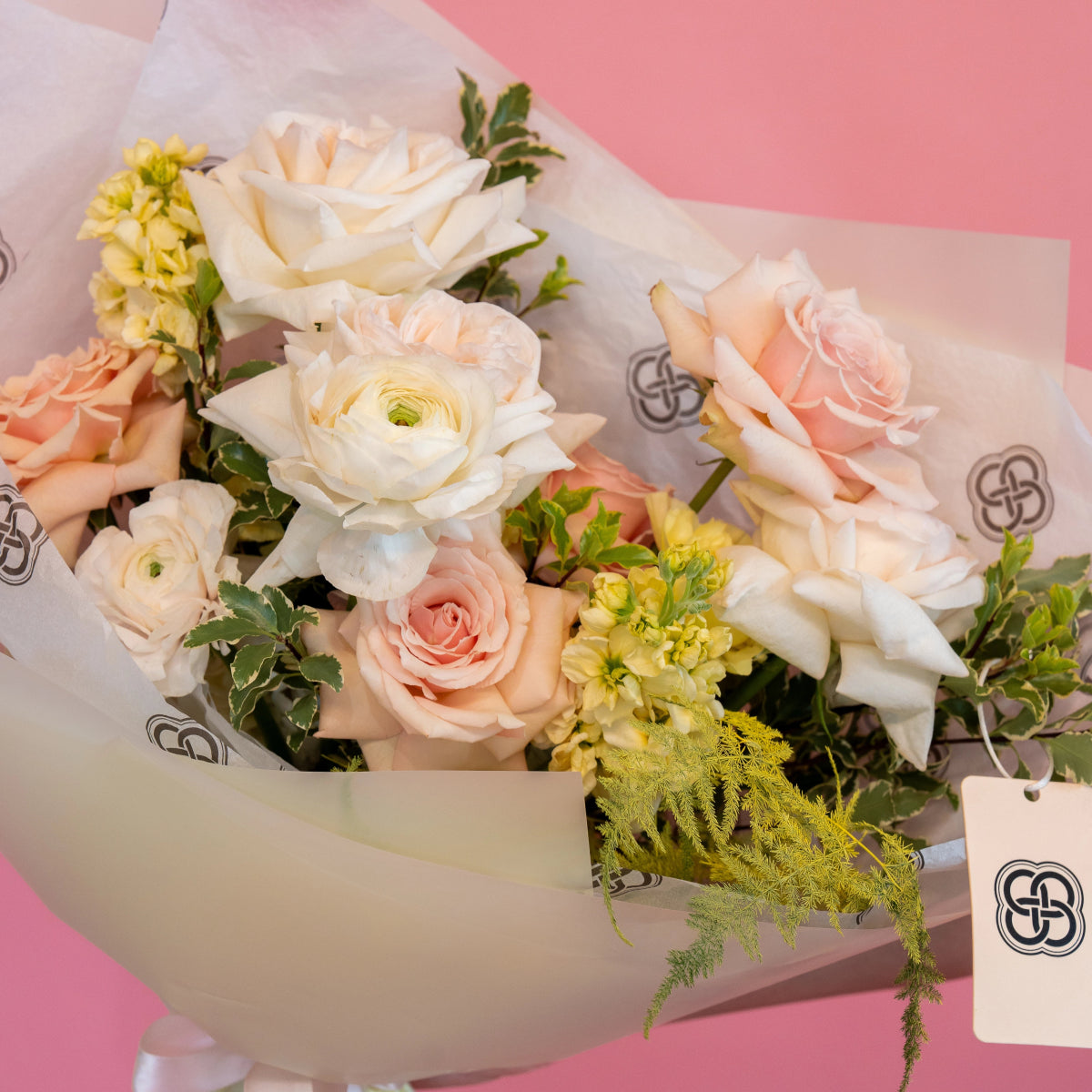 White and peach rose bouquet with ranunculus and yellow wildflowers in cream paper wrapping