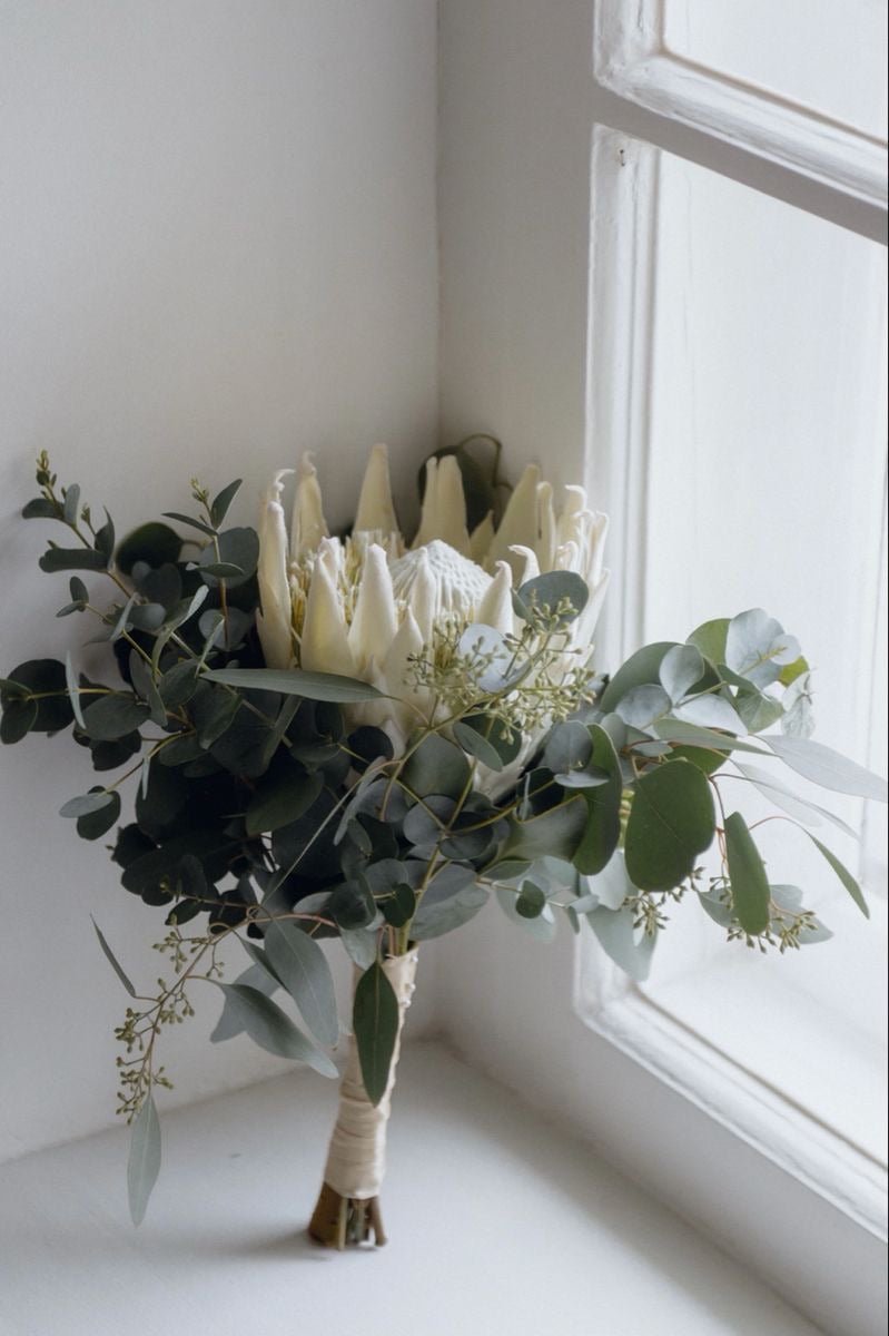 White protea bridal bouquet with eucalyptus greenery and ribbon wrap on windowsill
