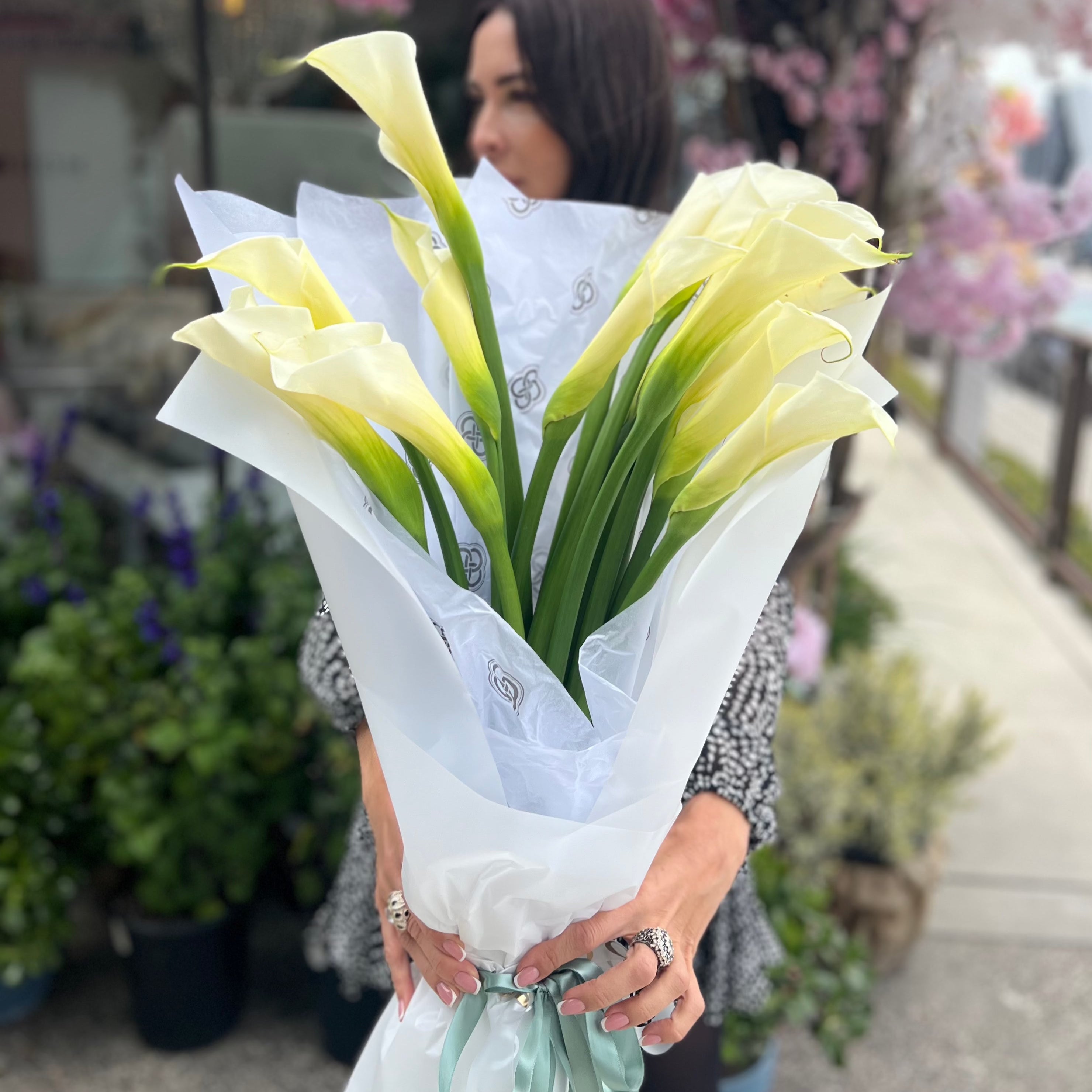Yellow calla lily bouquet wrapped in white paper with green ribbon held by woman at Los Angeles flower shop