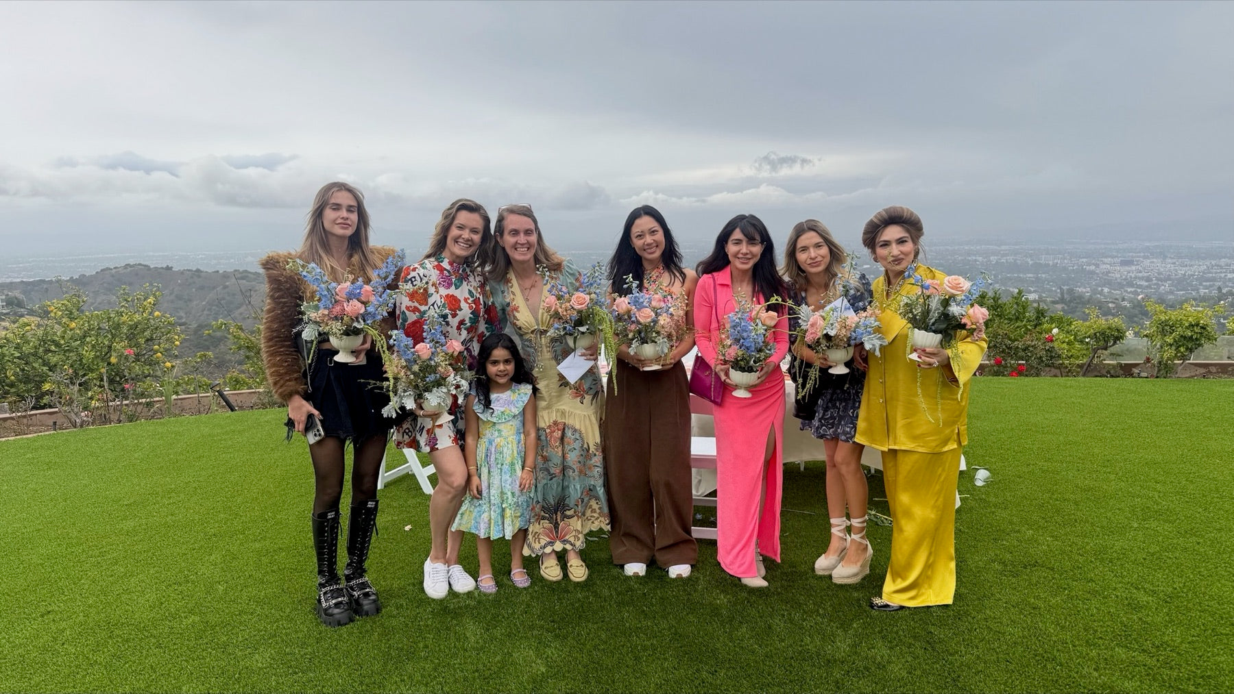 Guests on a hilltop lawn above Los Angeles, each holding a finished pastel flower arrangement.
